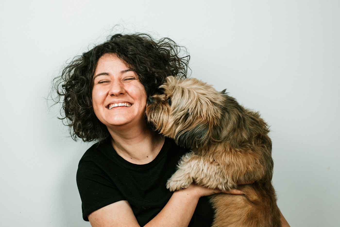 A woman laughing as her dog gives her a kiss